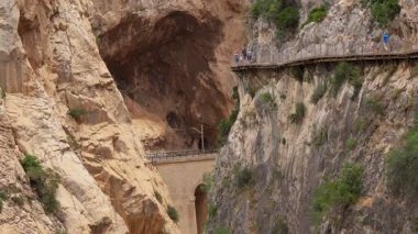 Yürüyüşçüler sarp kayalıklı duvarları olan bir kanyonun üzerinde dolambaçlı bir patikanın keyfini çıkarırlar, çarpıcı bir manzarada doğal güzellik ve macera sergilerler..