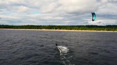 Uçurtma sörfçüsü, verimli yeşil ağaçlar ve kumlu kıyılarla çevrili sakin sularda ustalıkla manevra yapar..