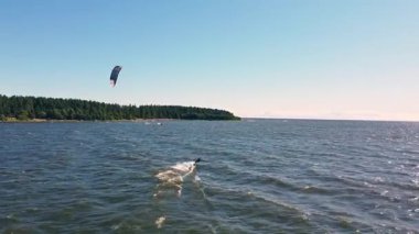 Heyecanlı bir uçurtma sörfçüsü günbatımında ormanlık bir sahil şeridinde parlayan sularda süzülürken adrenalin patlamasının tadını çıkarır..