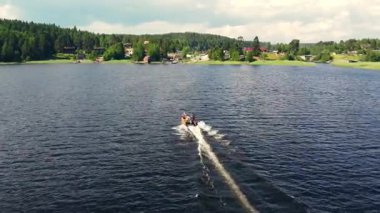 Bir grup arkadaş, dingin su ve yemyeşil manzaralarla çevrili, parlak bir gökyüzünün altındaki bir teknede heyecanlı bir gezinti yapıyorlar..