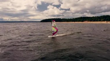 Becerikli bir rüzgar sörfçüsü, gür orman ve dramatik bulut oluşumlarıyla çevrili sakin sularda manevra yaparak açık hava sporlarının özünü yakalıyor..