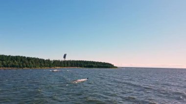 A kite surfer skillfully navigates the sparkling waters of a serene lake, surrounded by lush green trees under a clear sky.
