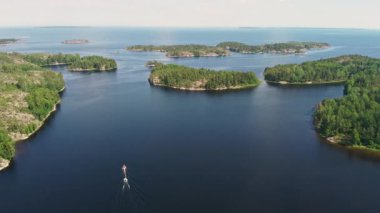 A tranquil boat glides through calm waters, surrounded by verdant islands, as the sun shines brightly on a beautiful day.