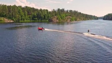 A thrilling water skiing experience unfolds under a bright sun, with lush greenery lining a peaceful lake in summer.