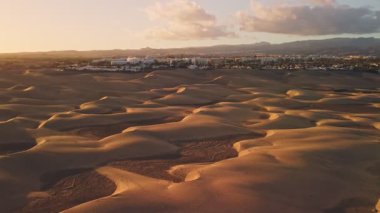 Altın kum tepeleri, hafif rüzgarlar tarafından şekillendirilmiş, sonsuz uzanır. Sakin bir kasaba, renkli bir günbatımı gökyüzünün altında uzanır..