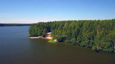 Serene göl kenarı, açık mavi gökyüzünün altında kumlu sahil ve canlı ormanlara ev sahipliği yapar. Rahatlama ve açık hava aktivitelerine davetiye çıkarır..