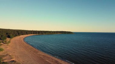 Yumuşak dalgalar alacakaranlıkta canlı bir gökyüzünün altında kumlu bir plaja doğru süzülür, yemyeşil ormanlar ve gölün sakin ufkuyla çerçevelenir..