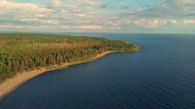 Güneş ışığı, yeşil ve sakin suları aydınlatırken, kumlu bir kıyıya doğru hafif dalgalar süzülür..