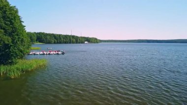 Bereketli ağaçlarla çevrili sakin bir göl açık mavi gökyüzünün altında süzülen renkli teknelere ev sahipliği yapar..