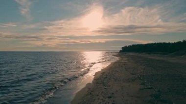 Gün batarken, gün ışığı sakin sularda parlıyor. Yumuşak dalgalar kumlu kıyıya çarpar ve barışçıl bir atmosfer yaratır..