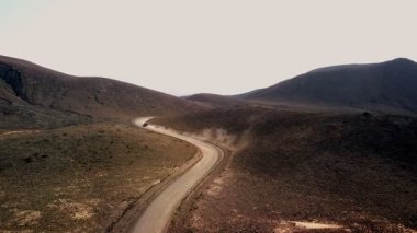 Toz bulutu, uçsuz bucaksız, kurak bir gökyüzü altında dolambaçlı bir yolda ilerlerken yükselir ve ıssız bir yerin güzelliğini gözler önüne serer..