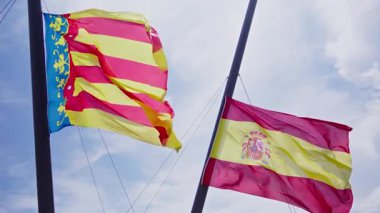 İspanya ve Valencia 'nın renklerini gösteren iki canlı bayrak, mavi gökyüzü ve bulutların arkaplanına karşı zarif bir şekilde havada süzülüyor..