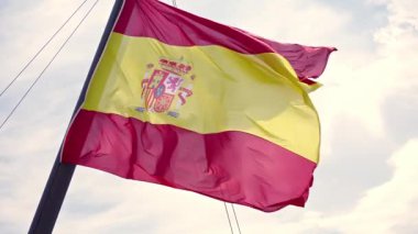 Titrek İspanyol bayrağı hafif meltemde cesurca dalgalanıyor, zengin renklerini ve amblemini gözler önüne seriyor, İspanya 'nın kimliğinin gerçek bir yansıması, açık bir arkaplan karşısında..