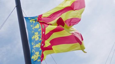 Canlı bir bayrak, mavi elementlerle birlikte sarı ve kırmızı şeritleri sergiliyor. Güneşli bir gökyüzünün altında enerjik bir şekilde dalgalanıyor. Kültürel kimliği ve yerel gururu simgeliyor..