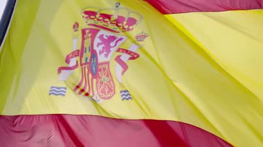 Renkli İspanyol bayrağı rüzgarda enerjik bir şekilde dalgalanıyor ulusal gururu somutlaştırıyor. Sahne, yerel bir olay sırasında parlak güneşin altında heyecan dolu bir anı yakalıyor..