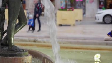 İnsanlar canlı meydanda yürürken çeşmeden zarif bir şekilde su sıçrıyor. Akşam manzarasının tadını çıkarıyorlar..