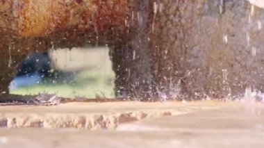 Parıldayan damlacıklar, açık havada sıcak güneş ışığıyla aydınlatılan dokulu taş bir yüzeye dökülüp sıçrıyor..