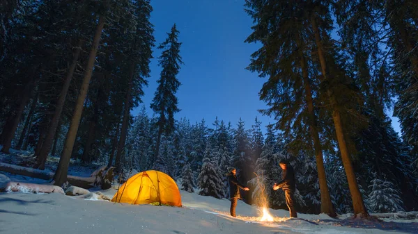 couple camping with campfire and tent outdoors in winter forest