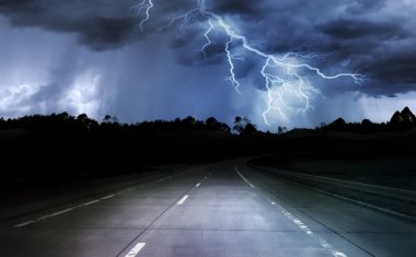 Karanlık gece yolu orman ve dağların arasından, yağmur ve yıldırımla fırtına