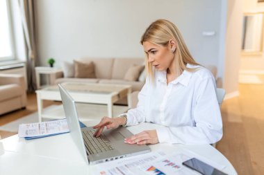 Uzaktan çalışma, teknoloji ve insan konsepti. Covid-19 sağlık krizi sırasında ev ofisinde çalışan bilgisayarlı ve evraklı mutlu gülümseyen genç iş kadını..