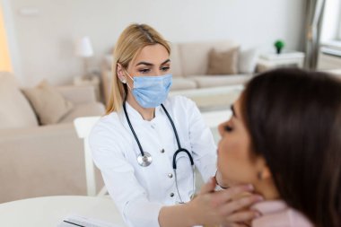Doktor boğazını muayene ederken genç bir kadın oturuyor. Doktor hasta tiroit bezini kontrol ediyor, hastanede sağlık muayenesi yapıyor.