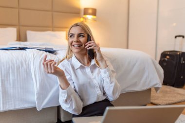 Otel odasından çalışan bir iş kadını. Güzel genç bir kadın cep telefonuyla konuşuyor. Yerde oturup iş seyahatinde eğlenmek.