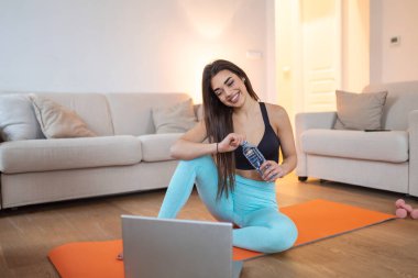 Kadın evde çalışıyor, antrenman yapıyor ve dizüstü bilgisayardan video izliyor. Güzel bir kadın egzersiz yapıyor. İnternette video izliyor ve görevlerini tekrarlıyor.