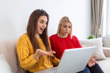 İki çekici kız, neşeli en iyi arkadaşlar, dizüstü bilgisayarda film izleyip evde kırmızı şarap içiyorlar. İki kadeh beyaz şarap.