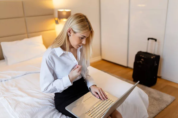 stock image Business woman getting comfortable after work, unbuttoning her shirt and looking at laptop. Businesswoman in hotel room on business trip