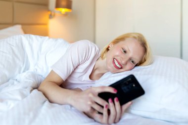 Genç, gülümseyen bir kadının fotoğrafı gece yatak odasında bir yatakta uzanırken görüntülü arama alır.