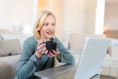 Positive young woman freelancer watching video in blog on netbook and having a coffee at comfortable home. Beautiful young business woman working on laptop.Freelancer connecting to internet