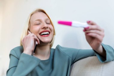 Smiling young woman looking on pregnancy test. Happy woman with pregnancy test. Smiling girl telling good news on mobile. Family, child expectation and maternity concept. Copy space