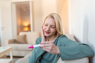 Young happy woman holding positive pregnancy test, shallow depth of field. Happy that she is going to have baby. Finally pregnant.
