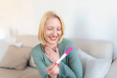 Young happy woman holding positive pregnancy test, shallow depth of field. Happy that she is going to have baby. Finally pregnant.