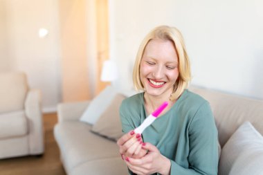 Young happy woman holding positive pregnancy test, shallow depth of field. Happy that she is going to have baby. Finally pregnant.