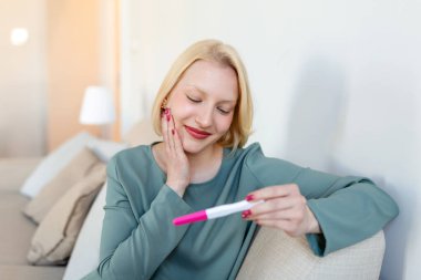 Young happy woman holding positive pregnancy test, shallow depth of field. Happy that she is going to have baby. Finally pregnant.