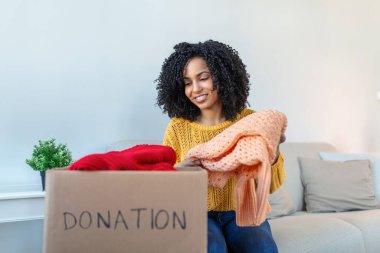 Woman holding cardboard donation box full with clothes. Concept of volunteering work, donation and clothes recycling. Helping poor people