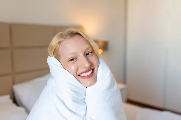 優しさを 白い毛布に包まれながら顔を笑顔にしている可愛い若い女性 ストックフォト — ストック写真