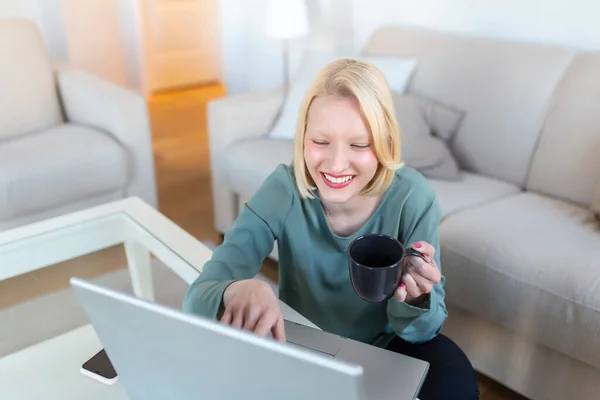 Positive young woman freelancer watching video in blog on netbook and having a coffee at comfortable home. Beautiful young business woman working on laptop.Freelancer connecting to internet