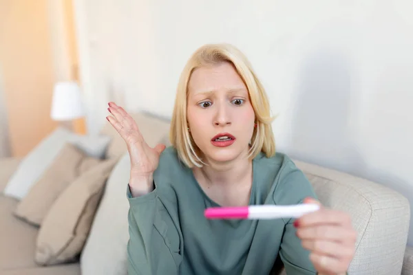 Sad, worried woman checking her recent pregnancy test, sitting on couch at home. Maternity, child birth and family problems concept. unwanted pregnancy