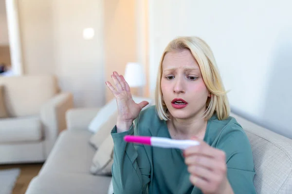 忧心忡忡的女人检查她最近的怀孕测试 坐在家里的沙发上 分娩和家庭问题概念 意外怀孕 — 图库照片