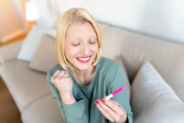幸せの妊娠検査を見ている若い女性 やっと妊娠した 自宅でソファに座っている間に妊娠検査と笑顔を見て魅力的な女性 — ストック写真