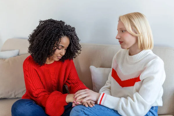 Friend trying to calm down her friend. Woman crying. Young lady sharing her problem with friend. female in depression. Woman omforting hes sad friend sitting on a couch in the living room at home