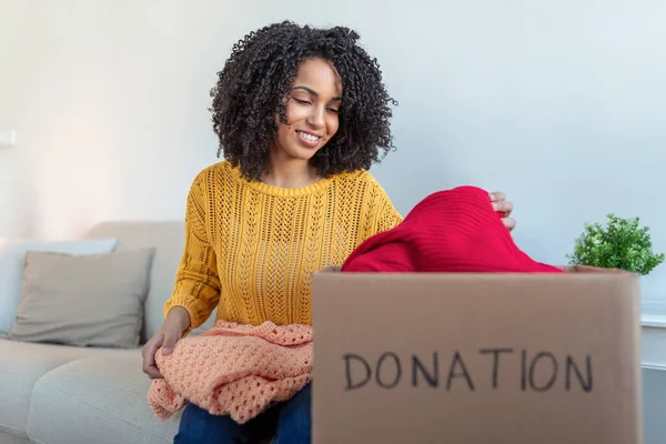 Donation Concept. Woman holding a Donate Box with full of Clothes. Woman holding a book and clothes donate box. Clothes in box for concept donation and reuse recycle