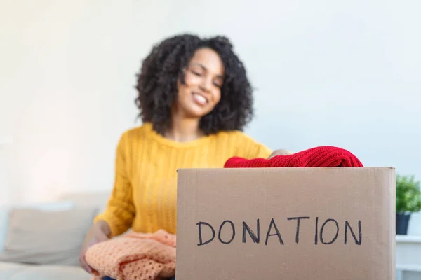 Donation Concept. Woman holding a Donate Box with full of Clothes. Woman holding a book and clothes donate box. Clothes in box for concept donation and reuse recycle