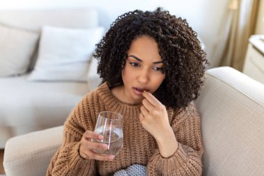 Korkunç acıdan acı çekme kavramı. Güzel, üzgün, üzgün, mutsuz, sorunlu, siyah saçlı, sıradan kıyafetler giyen zayıf kadın bir kanepede oturup hap alıyor.