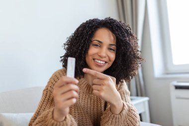 Negatif bir test cihazını tutan Afro-Amerikalı kadının yakın plan fotoğrafı. Negatif Coronavirus 'unu gösteren mutlu genç kadın - Covid-19 hızlı testi. Teste odaklan. Coronavirüs.