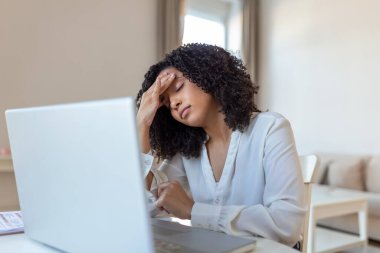 Yorgun iş kadınının ev ofisinde başı ağrıyor. Ofis masasında çalışan Afrikalı Amerikalı yaratıcı kadın yorgun hissediyor. Stresli iş kadını çok çalışırken göz ağrısı çekiyor