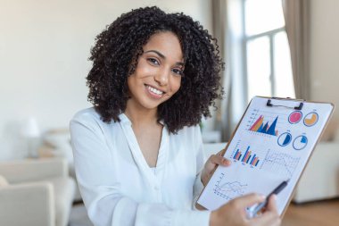 Uzaktan çalışma, teknoloji ve insan konsepti. Covid-19 sağlık krizi sırasında ev ofisinde çalışan bilgisayarlı ve evraklı mutlu gülümseyen genç iş kadını..