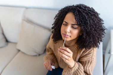 Evde koronavirüs PCR testi yaparken pamuk çubuğu kullanan Afro-Amerikalı bir kadın. Coronavirus hızlı tanı testi uygulayan bir kadın. Evde genç bir kadın COVID-19 için burun çubuğu kullanıyor..
